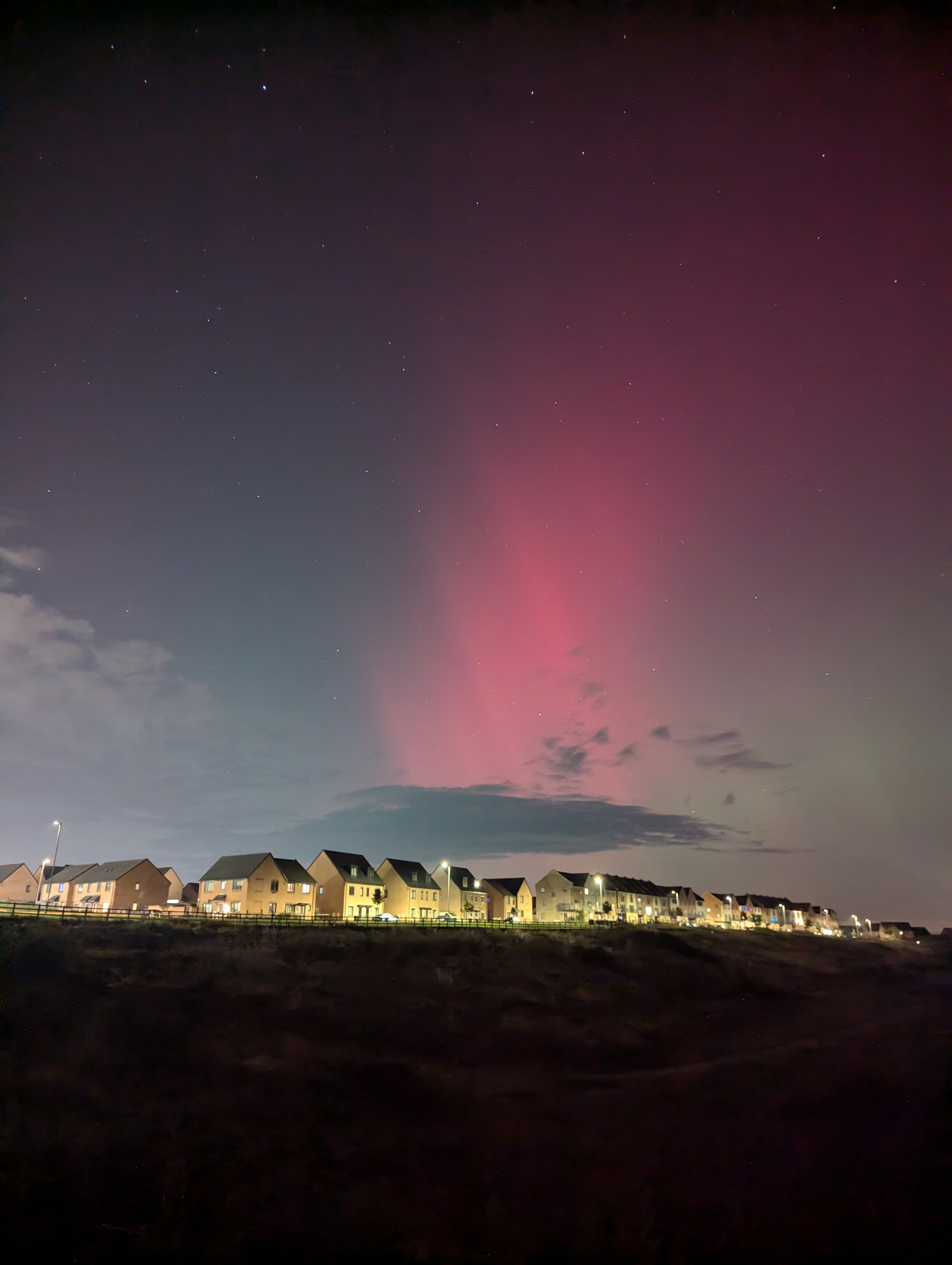 Red aurora above a row of houses with light cloud at the horizon. East Midlands, UK. 10th October 2024.